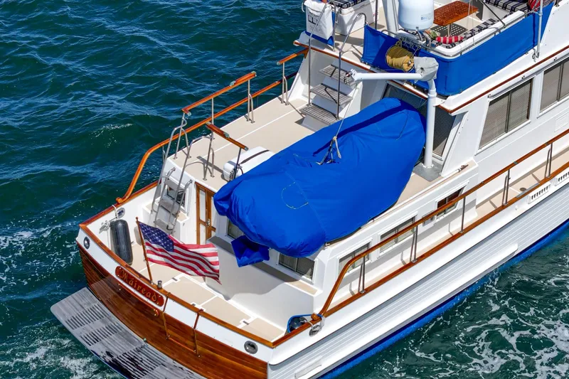 Slide: The Image of 1987 Grand Banks 46 Classic yacht with blue cover, American flag, cruising on open water. - 3