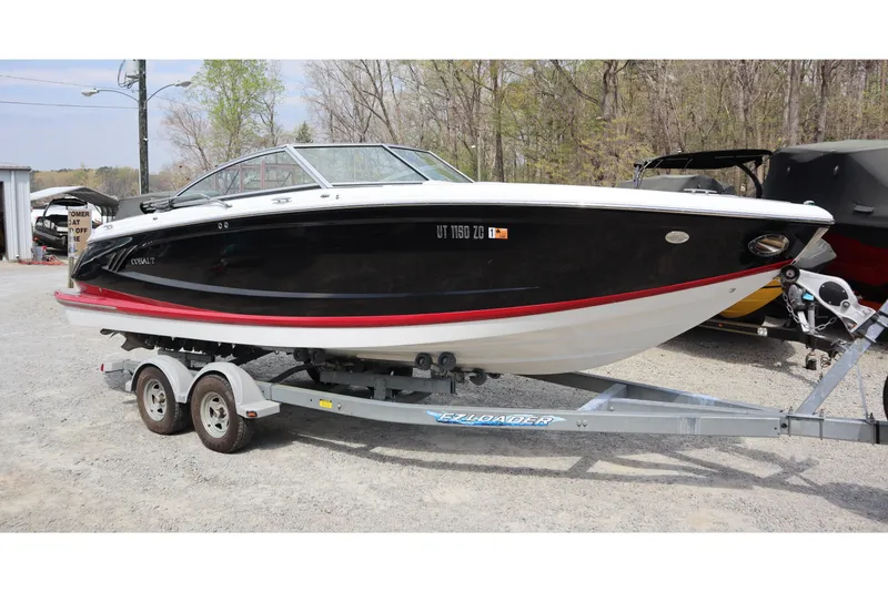 Slide: The Image of 2012 Cobalt A25 boat on trailer, black and white with red trim, parked outdoors. - 0