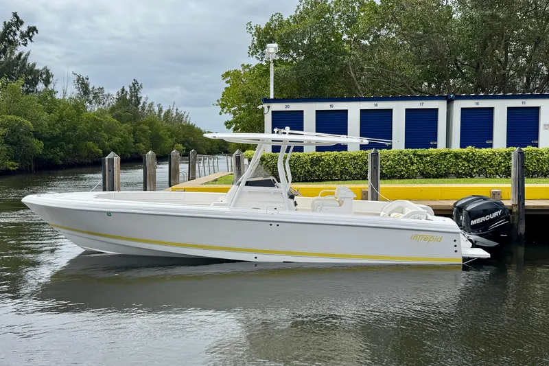 Slide: The Image of 2013 Intrepid 300 Center Console boat docked by storage units and greenery. - 2