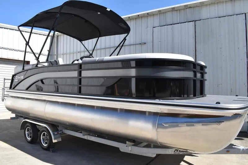 The Image of 2026 Lowe SS 230 pontoon boat with canopy on trailer, parked near metal building. - 0