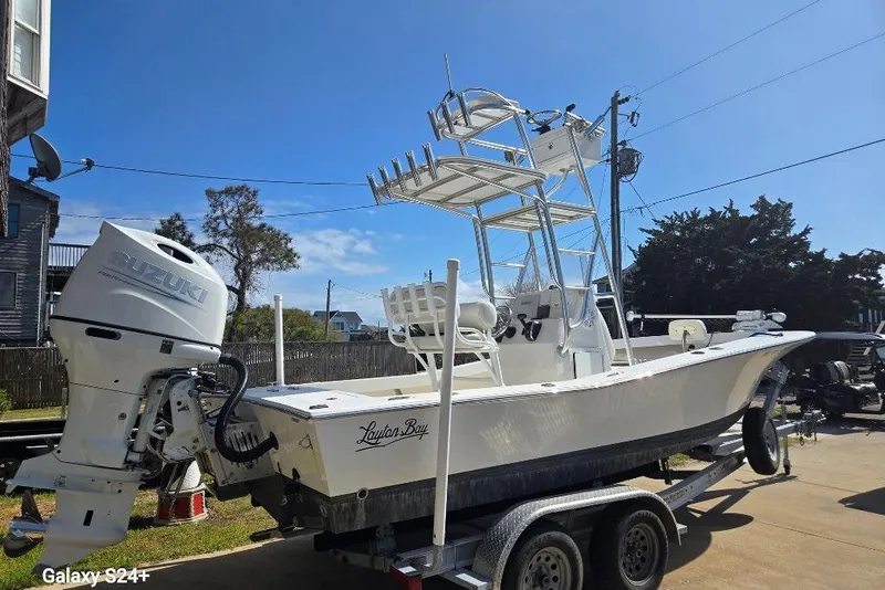 Slide: The Image of 2023 Layton Bay 22 boat with Suzuki outboard motor on a trailer, under clear blue sky. - 2