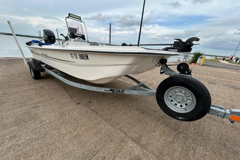 The Image of 2018 Mako Pro Skiff 17 CC boat on trailer by waterfront, overcast sky. - 0