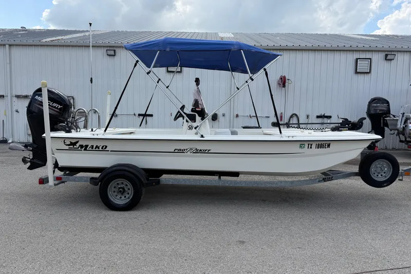 Slide: The Image of 2018 Mako Pro Skiff 17 CC boat with blue canopy on trailer, parked outdoors. - 14