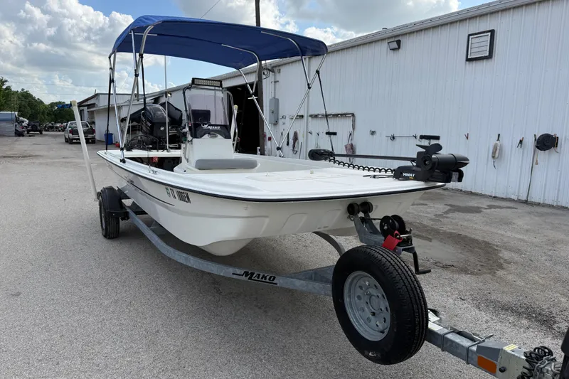 Slide: The Image of 2018 Mako Pro Skiff 17 CC boat with blue canopy on trailer, parked outside. - 17