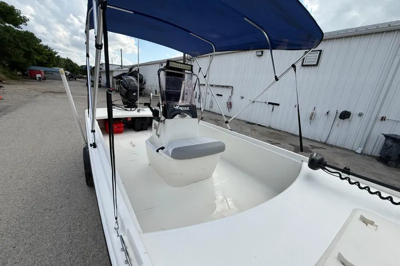 Slide: The Image of 2018 Mako Pro Skiff 17 CC boat with blue canopy, parked near a white building. - 21