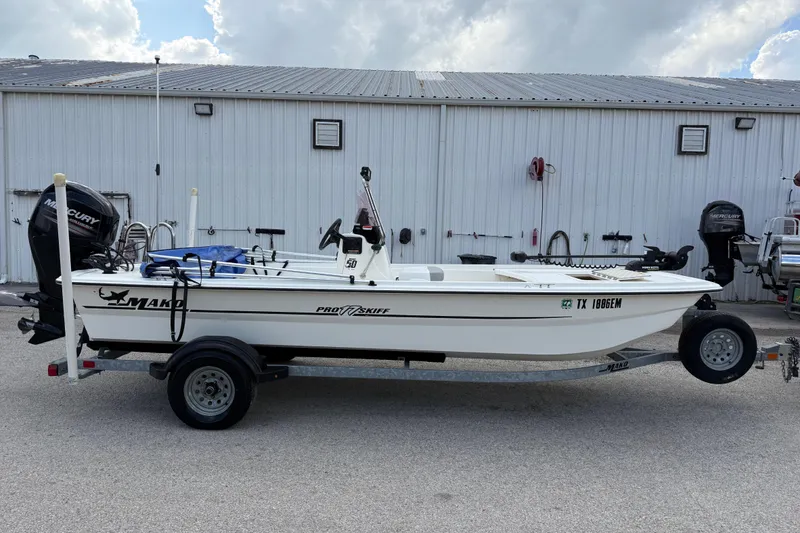 Slide: The Image of 2018 Mako Pro Skiff 17 CC boat on trailer, parked outside a metal building. - 39
