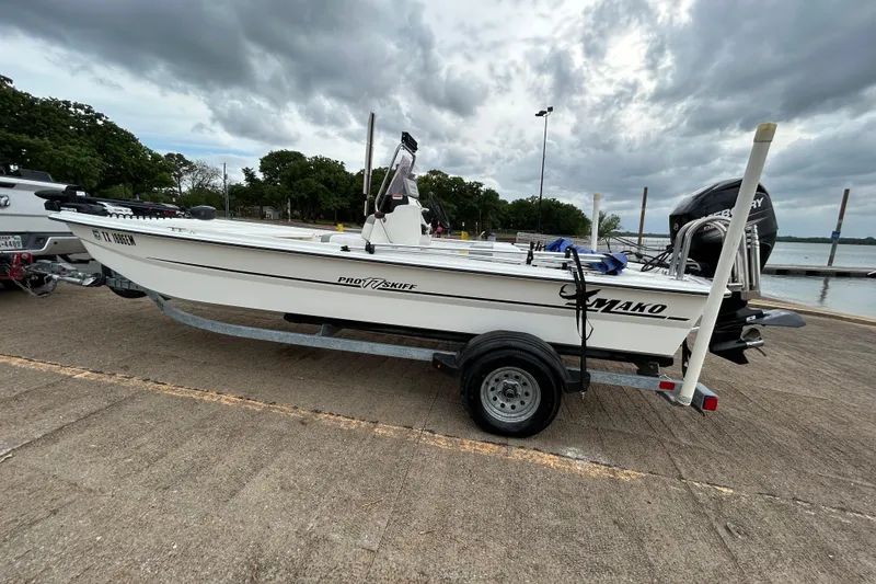 Slide: The Image of 2018 Mako Pro Skiff 17 CC boat on trailer by lakeside under cloudy sky. - 50