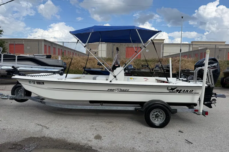 Slide: The Image of 2018 Mako Pro Skiff 17 CC boat with blue canopy on trailer, parked outdoors. - 6