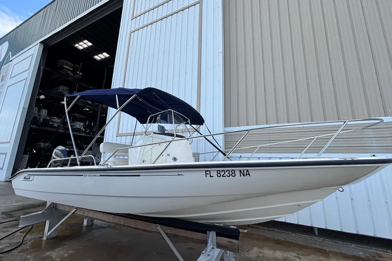 The Image of 2005 Boston Whaler 220 Dauntless boat with blue canopy, docked near a large warehouse. - 0