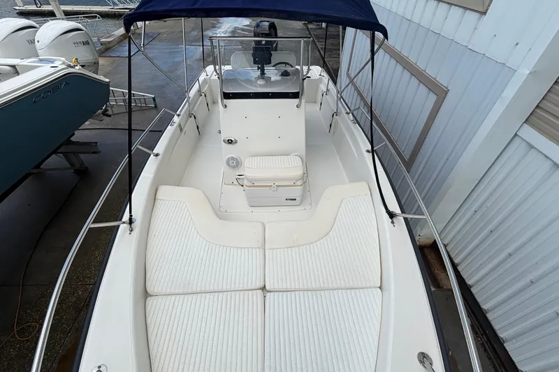 Slide: The Image of 2005 Boston Whaler 220 Dauntless boat with seating and console, docked near other vessels. - 14
