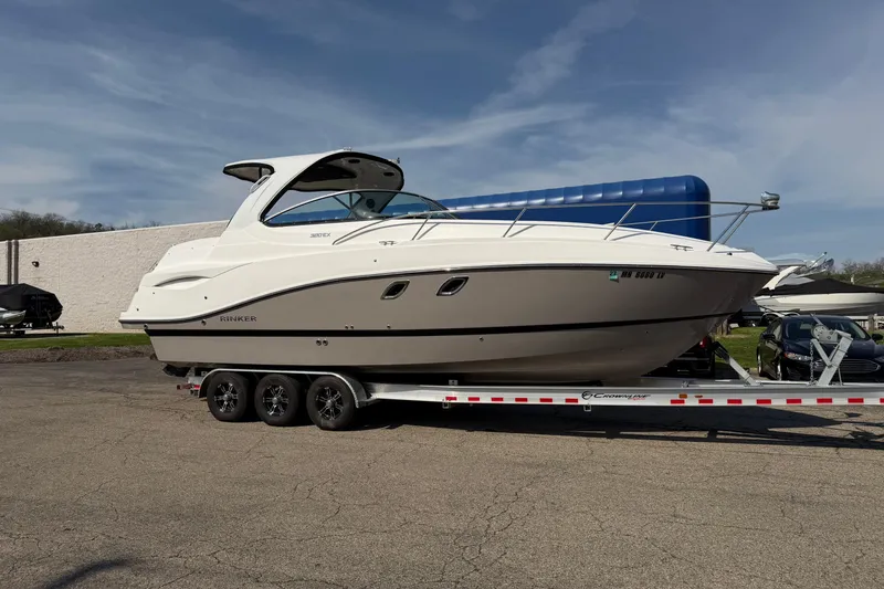 The Image of 2019 Rinker EX 320 boat on a trailer, parked outdoors under a clear sky. - 0