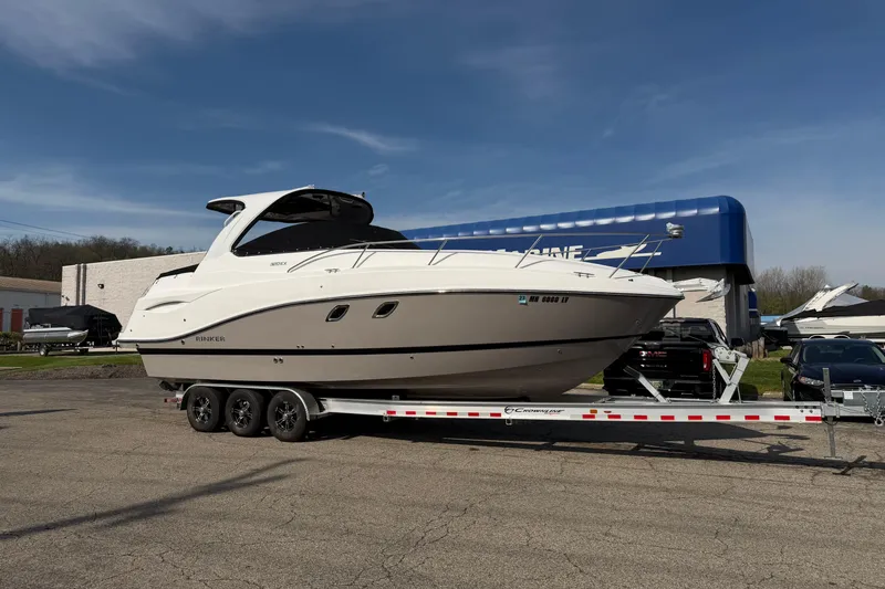Slide: The Image of 2019 Rinker EX 320 boat on trailer, parked outdoors under clear blue sky. - 67