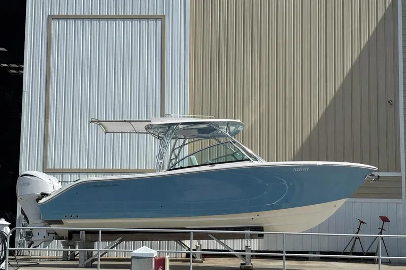 The Image of 2023 Cobia 280 Dual Console boat in blue, docked near a large building. - 0