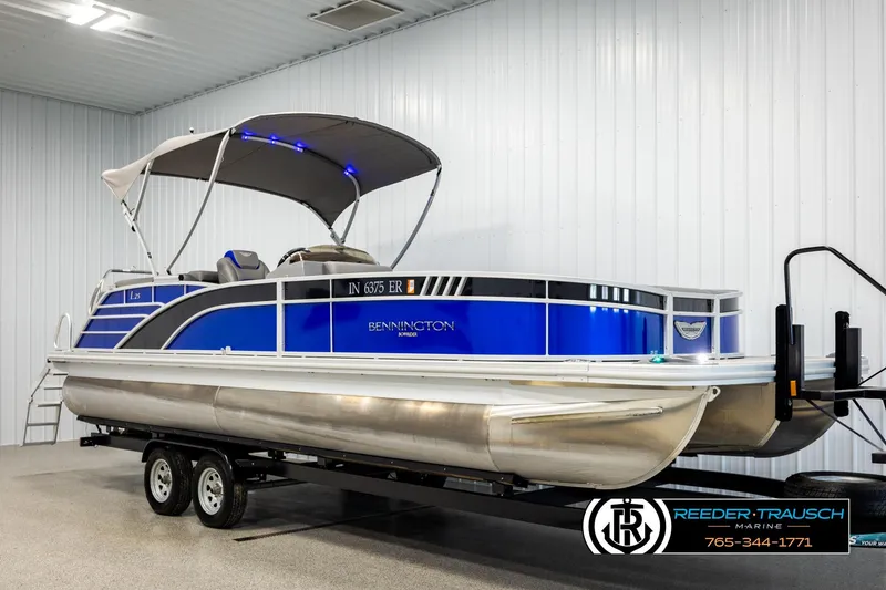 Slide: The Image of 2025 Bennington LTFBSE pontoon boat with blue accents on a trailer in a showroom. - 3