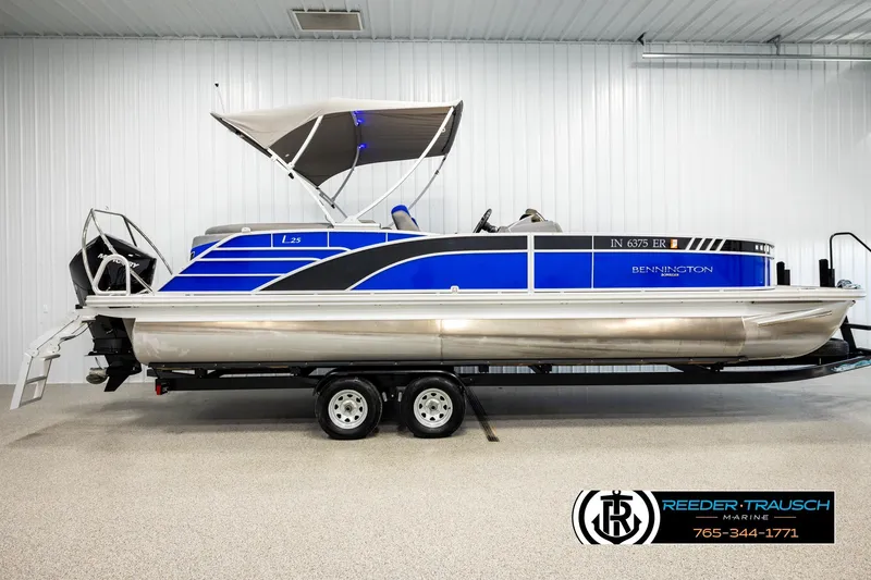 Slide: The Image of 2025 Bennington LTFBSE pontoon boat with blue accents on a trailer in a showroom. - 5
