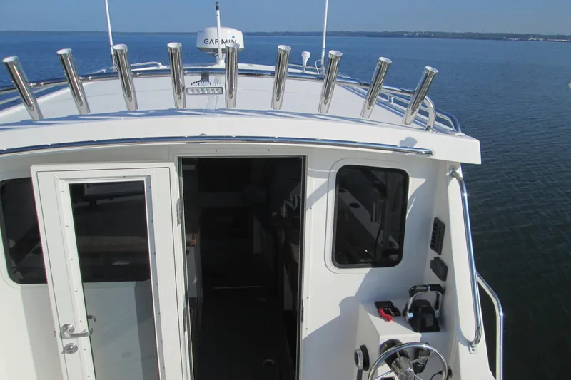 Slide: The Image of 2026 Seaport Commander 2800 boat cockpit with steering wheel and rod holders on calm water. - 25