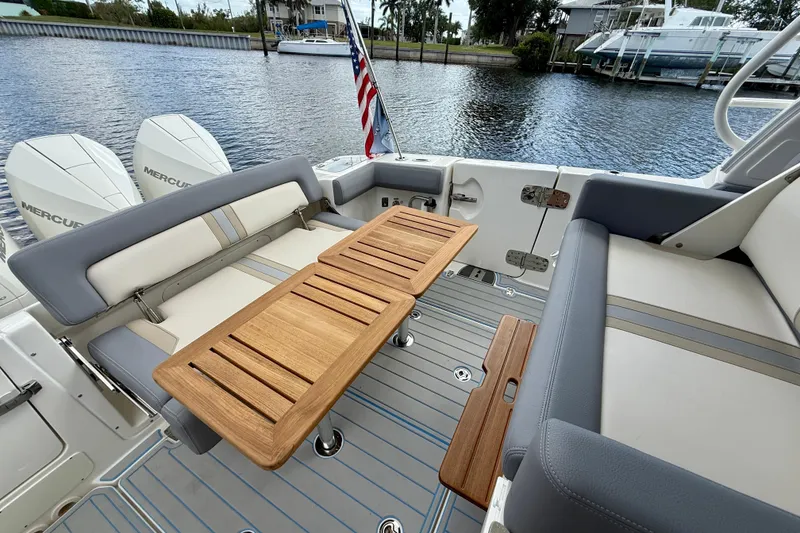 Slide: The Image of 2025 Boston Whaler 350 Realm boat interior with wooden table and seating by the water. - 23