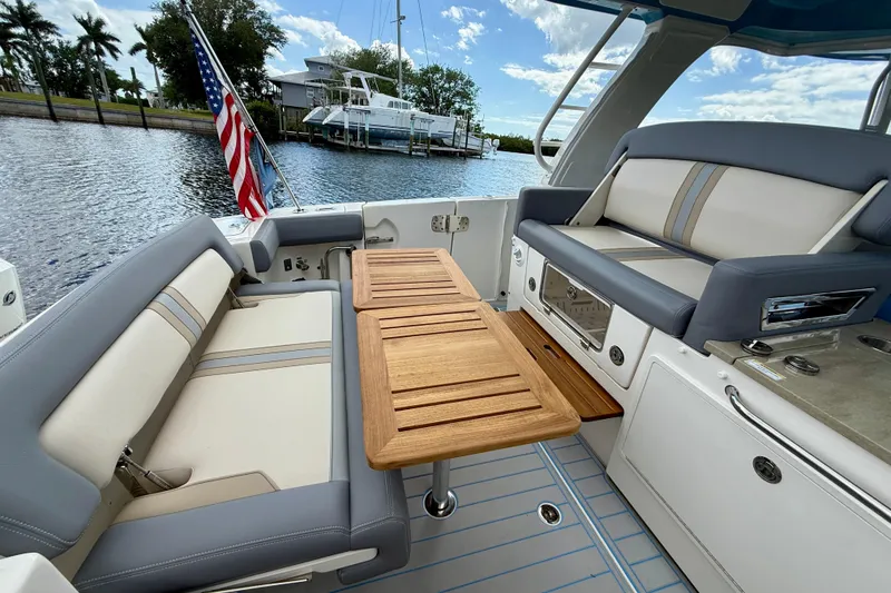 Slide: The Image of 2025 Boston Whaler 350 Realm boat interior with seating and wooden table, docked by water. - 24