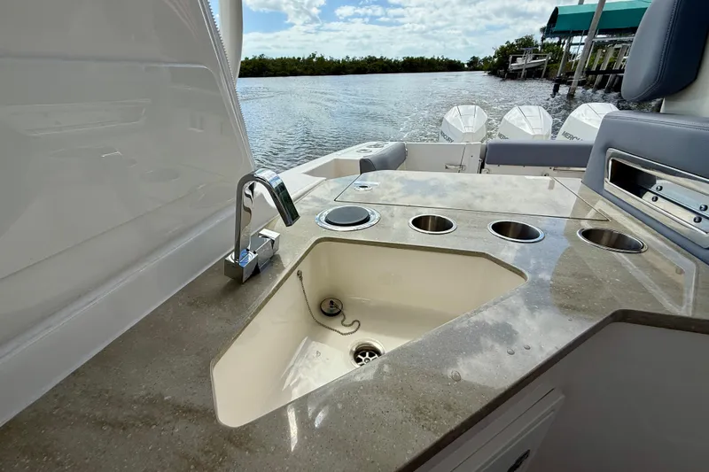 Slide: The Image of 2025 Boston Whaler 350 Realm boat sink and countertop with cup holders, docked by water. - 30