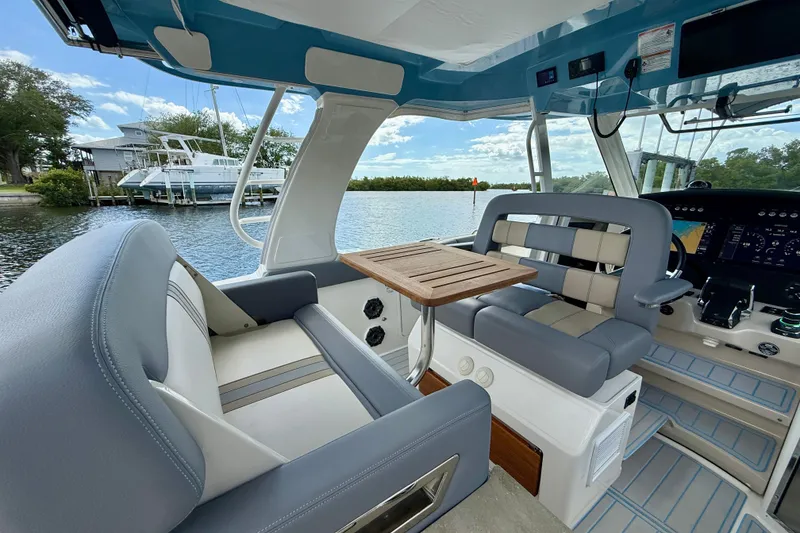 Slide: The Image of 2025 Boston Whaler 350 Realm interior with seating and table, docked by the water. - 34