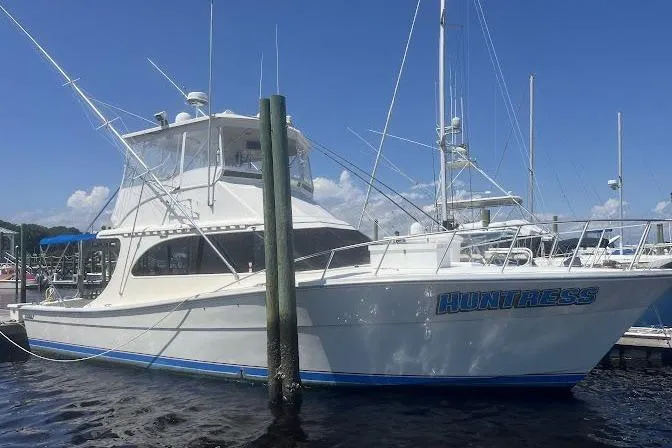 The Image of 1989 Topaz 44 Sportfisherman boat docked, named "Huntress," under a clear blue sky. - 1