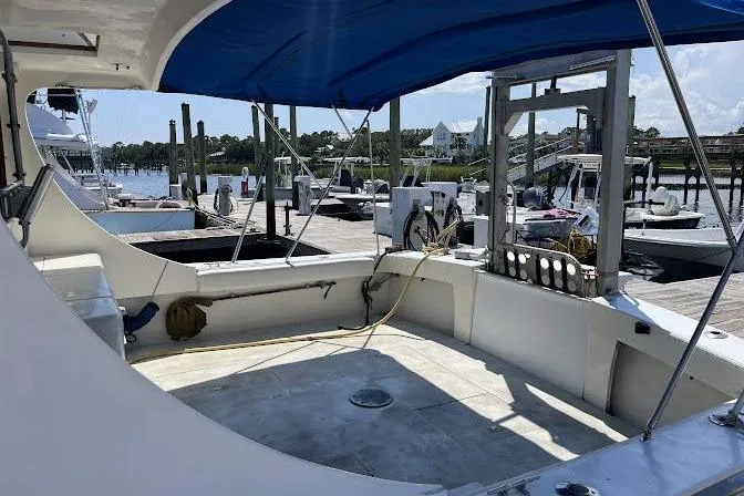 Slide: The Image of 1989 Topaz 44 Sportfisherman boat docked, featuring spacious deck and blue canopy. - 6