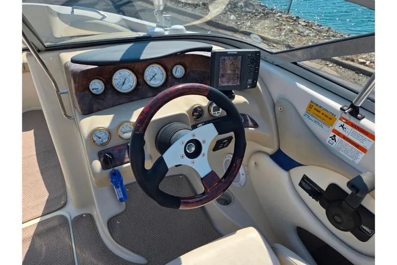 Slide: The Image of 2005 Glastron GX 235 boat dashboard with steering wheel and gauges, overlooking water. - 13