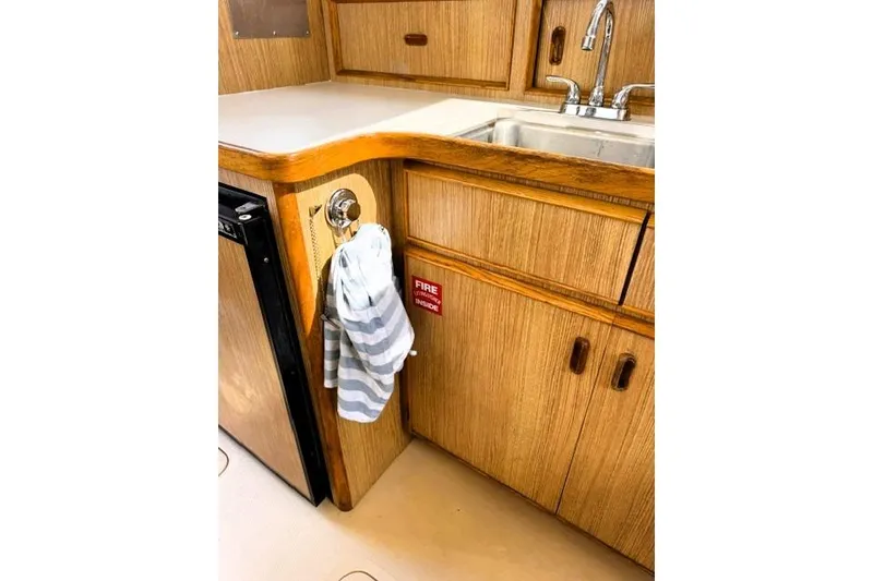 Slide: The Image of 1991 Bertram 28 boat kitchen with wooden cabinets, sink, and striped towel. - 26