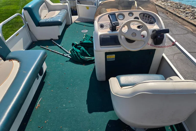 Slide: The Image of 1998 Starcraft boat interior with green carpet, steering wheel, and seating near a lakeside. - 17