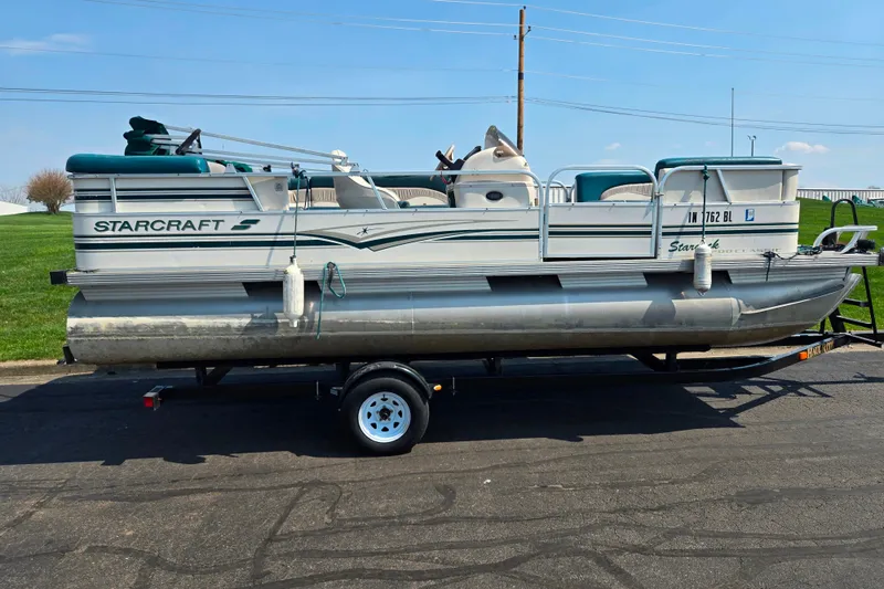 Slide: The Image of 1998 Starcraft pontoon boat on trailer, parked on asphalt, with green and white accents. - 4