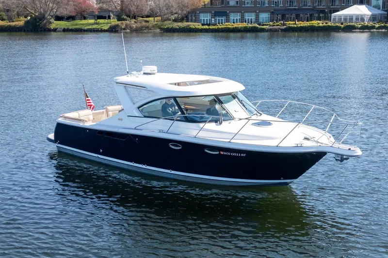 Slide: The Image of 2014 Tiara Yachts 3100 Coronet cruising on a serene lake near modern buildings. - 3