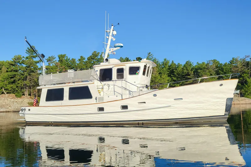 The Image of Hans Christian 1990 Independence yacht on calm water, surrounded by lush greenery. - 0