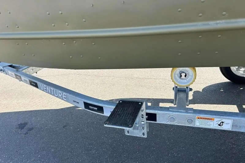 Slide: The Image of 2024 Lund UR1448MTD boat on Venture trailer, close-up of hull and wheel. - 14