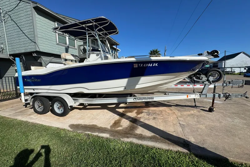 The Image of 2016 NauticStar 231 Coastal boat on trailer, parked in driveway under clear blue sky. - 0