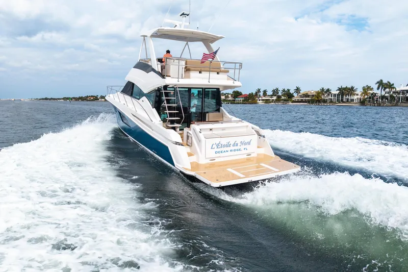 Slide: The Image of 2015 Tiara Yachts cruising on water, rear view with American flag, coastal homes in background. - 11
