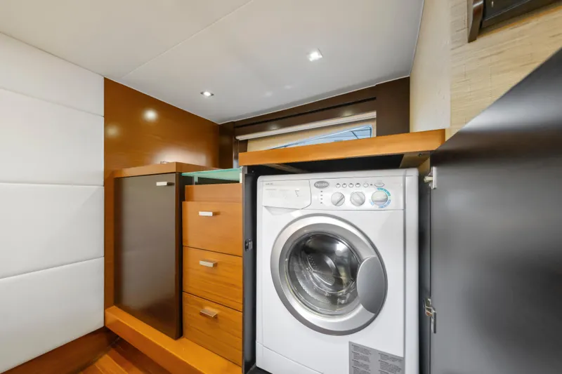 Slide: The Image of Laundry area inside a 2015 Tiara Yacht, featuring a washing machine and wooden cabinetry. - 54