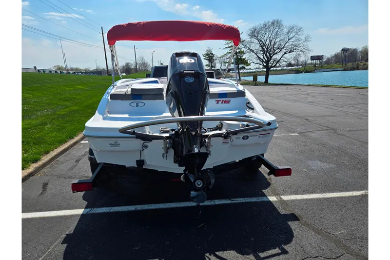 Slide: The Image of 2024 Tahoe T16 boat with red canopy, parked near a lake on a sunny day. - 2