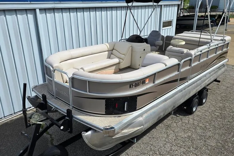 The Image of 2007 South Bay 8522 CR E series pontoon boat on trailer, parked by metal building. - 0