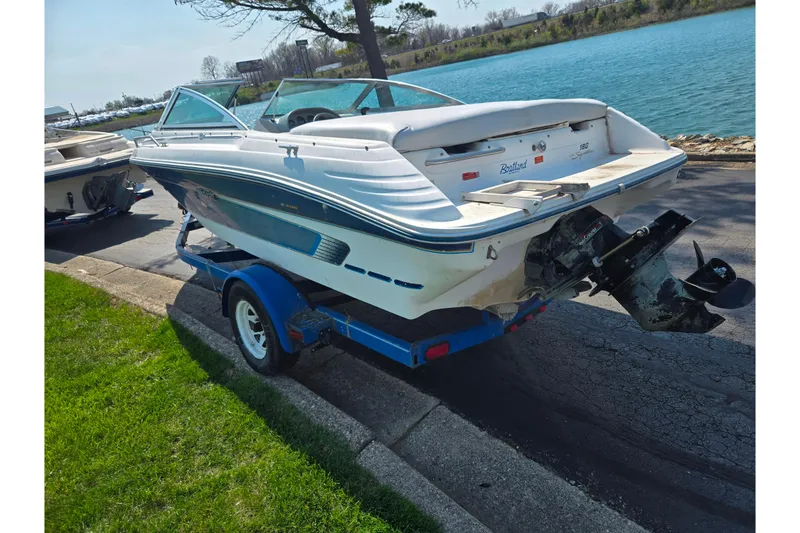 Slide: The Image of 1994 Sea Ray 180 Bow Rider on trailer by a lakeside road. - 2