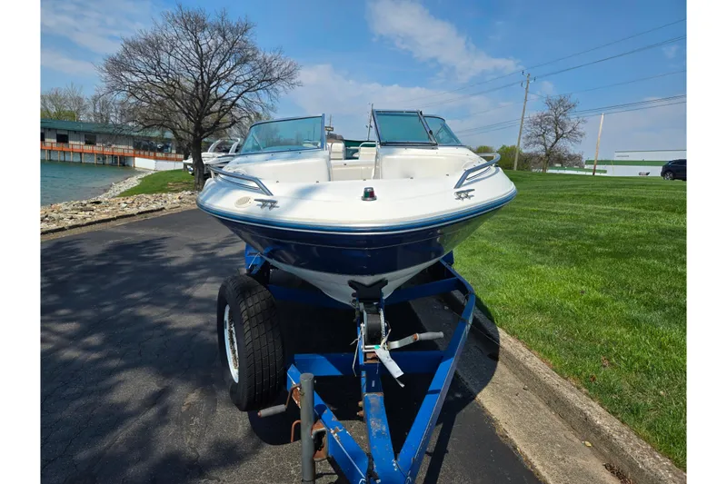 Slide: The Image of 1994 Sea Ray 180 Bow Rider on trailer, parked near a lake under a clear blue sky. - 7