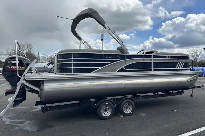 The Image of 2022 Bennington L 23 L-Bench pontoon boat on trailer, under cloudy sky. - 0