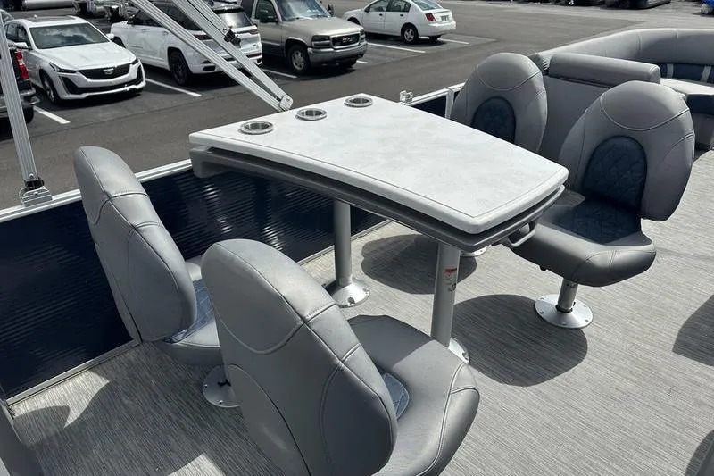 Slide: The Image of 2022 Bennington L 23 L-Bench boat interior with gray seating and table in a parking lot. - 14