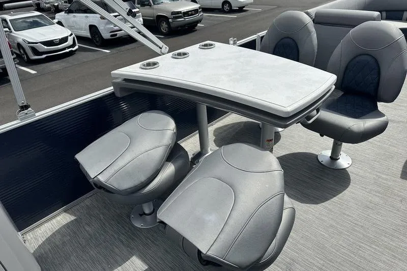 Slide: The Image of 2022 Bennington L 23 L-Bench boat interior with gray seating and table in a parking lot. - 8