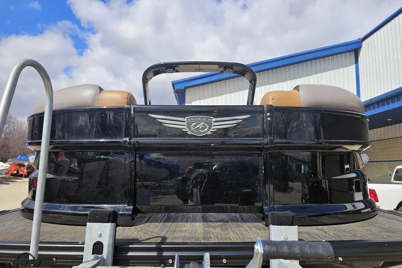 Slide: The Image of 2024 Avalon Excalibur Quad Lounge Windshield boat, black exterior, parked outdoors under a cloudy sky. - 17
