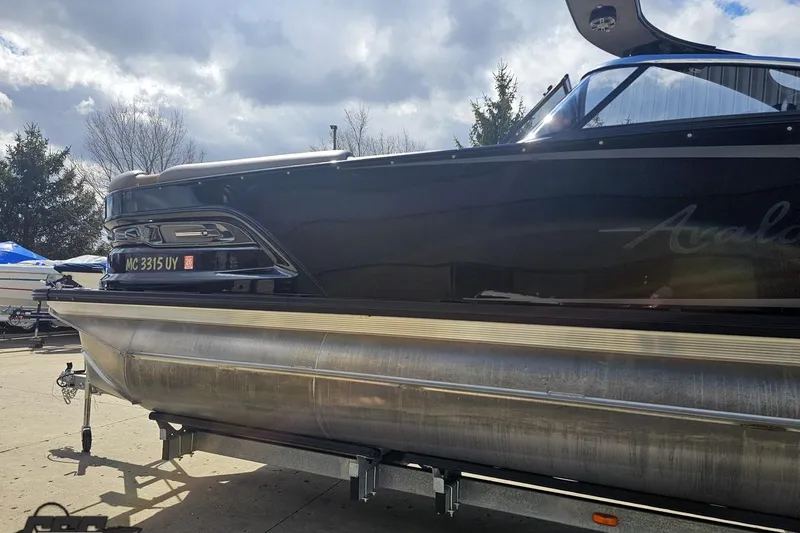Slide: The Image of 2024 Avalon Excalibur Quad Lounge Windshield boat on trailer under cloudy sky. - 26