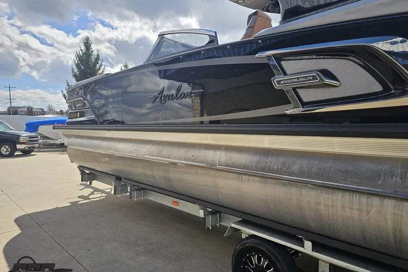 Slide: The Image of 2024 Avalon Excalibur Quad Lounge Windshield boat on trailer under cloudy sky. - 34