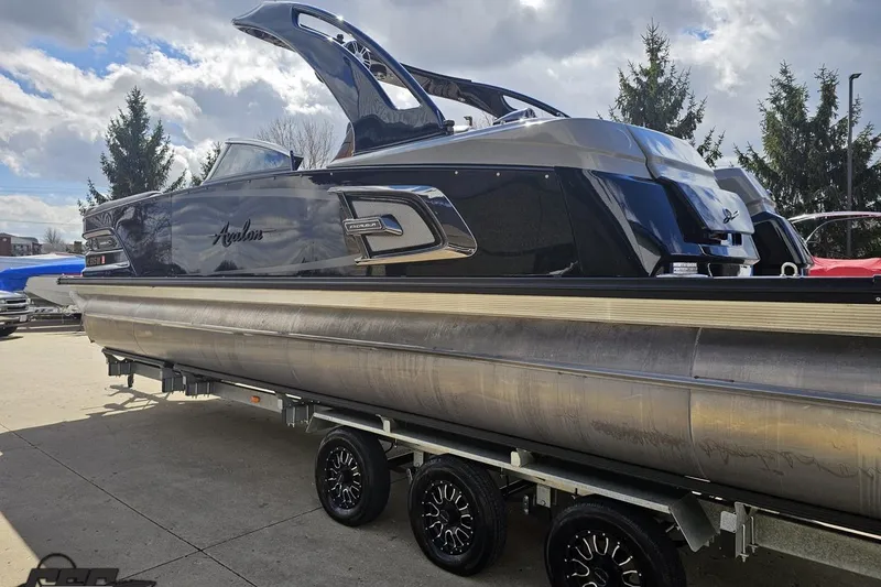 Slide: The Image of 2024 Avalon Excalibur Quad Lounge Windshield boat on trailer under cloudy sky. - 35