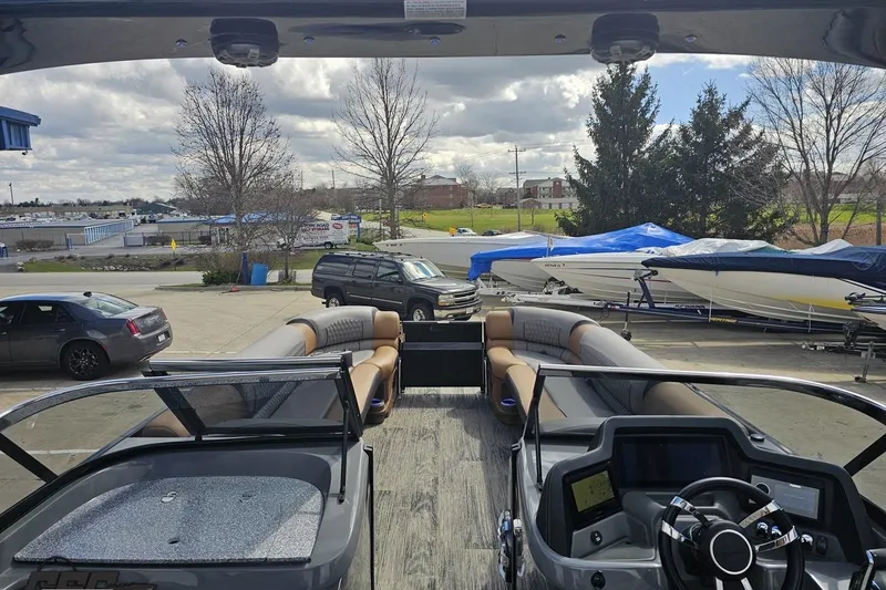 Slide: The Image of 2024 Avalon Excalibur Quad Lounge boat interior with windshield, parked near covered boats. - 67