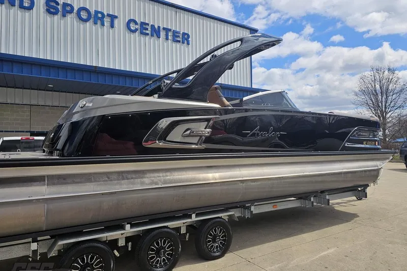 Slide: The Image of 2024 Avalon Excalibur Quad Lounge Windshield boat on trailer at sport center. - 7