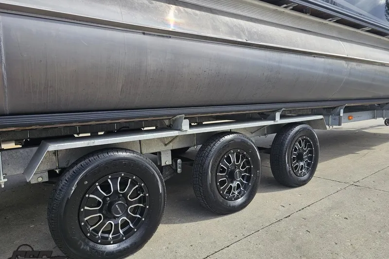 Slide: The Image of 2024 Avalon Excalibur Quad Lounge Windshield boat on trailer with stylish black wheels. - 9